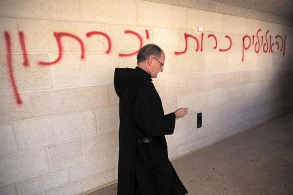 A priest walks past a graffiti reading in Hebrew “idols will be cast out” as he inspects the damage at the Church of the Multiplication at Tabgha, on the shores on the Sea of Galilee in northern Israel, on June 18, 2015 AFP PHOTO / MENAHEM KAHANA